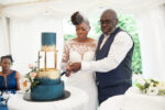 A couple cutting a teal and gold wedding cake in a marquee at a Nigerian wedding reception in Hertfordshire