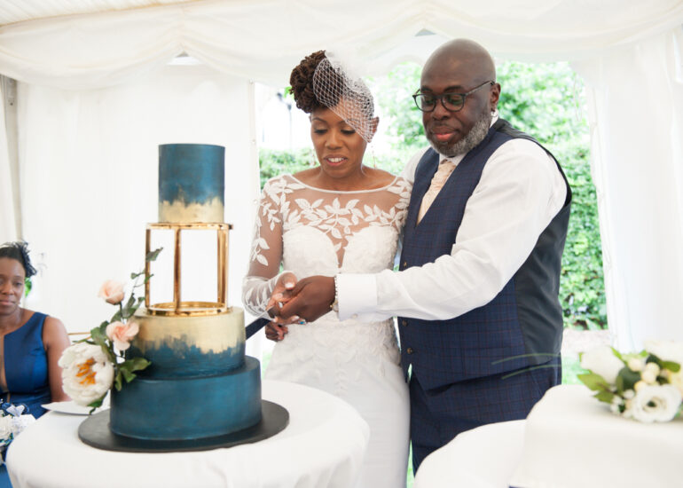 A couple cutting a teal and gold wedding cake in a marquee at a Nigerian wedding reception in Hertfordshire