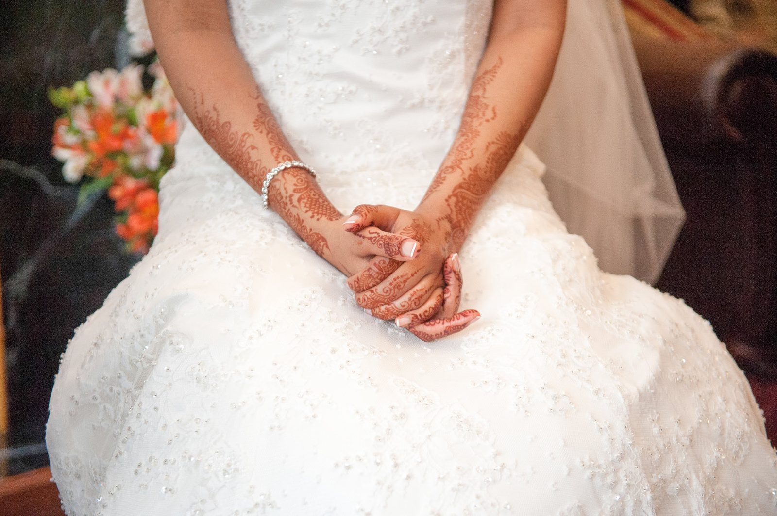 The bride in a white lace gown holding her hands together, henna on her palms, before a church wedding ceremony