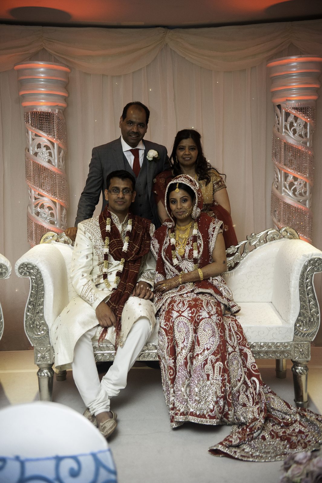 The couple seated on the reception stage in traditional red and cream dress at an Asian wedding