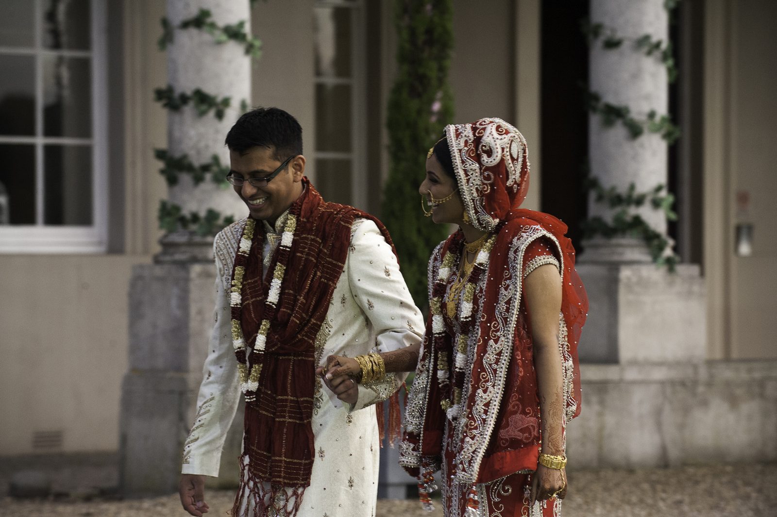 The couple in traditional dress wearing varmala flower garlands, walking together outside the reception venue