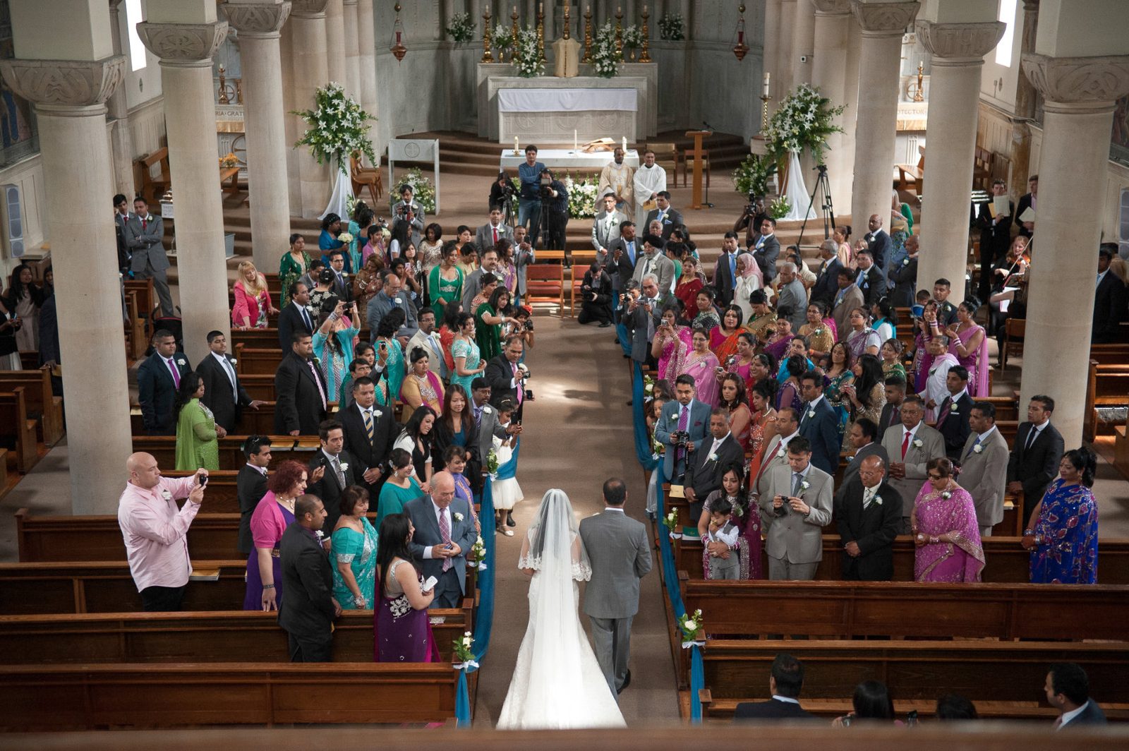 A full church of guests in saris and suits as the bride walks the aisle at an Indian Christian wedding