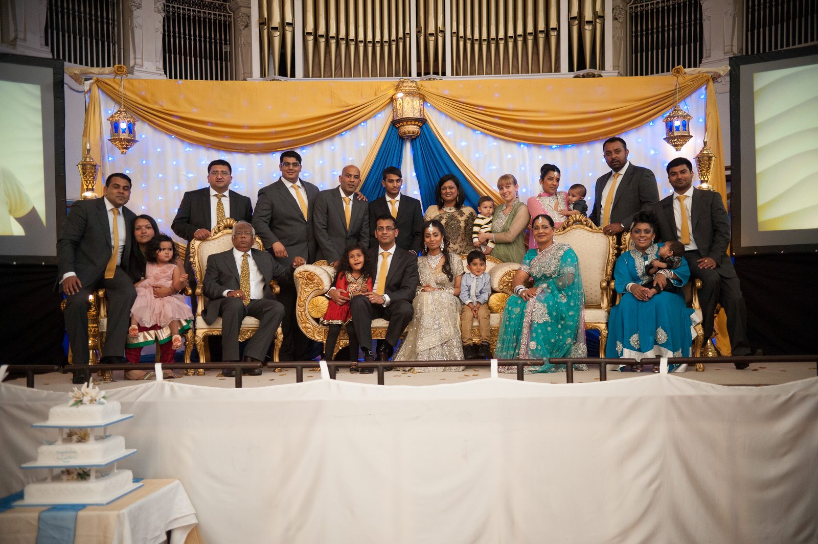 The reception hall stage with gold thrones, blue and gold drapes and the cake at an Asian wedding