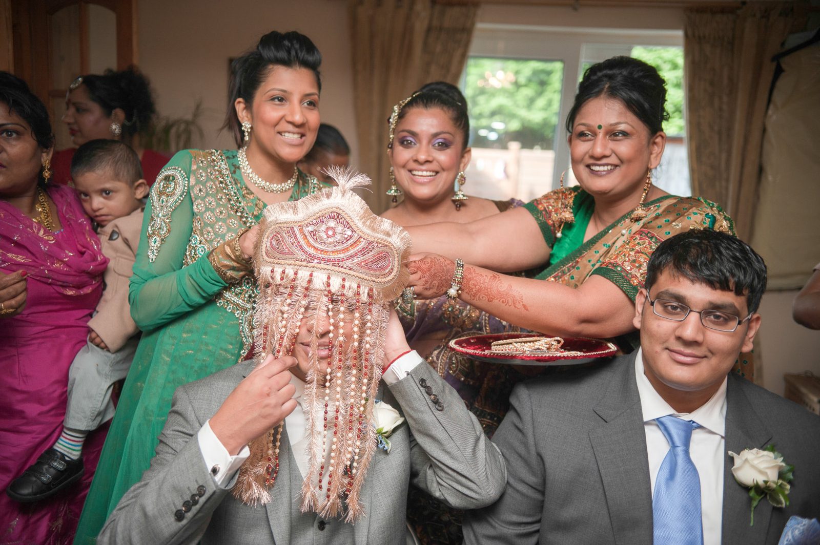 The groom receiving sweets and a garland from family before leaving for the church at an Asian wedding